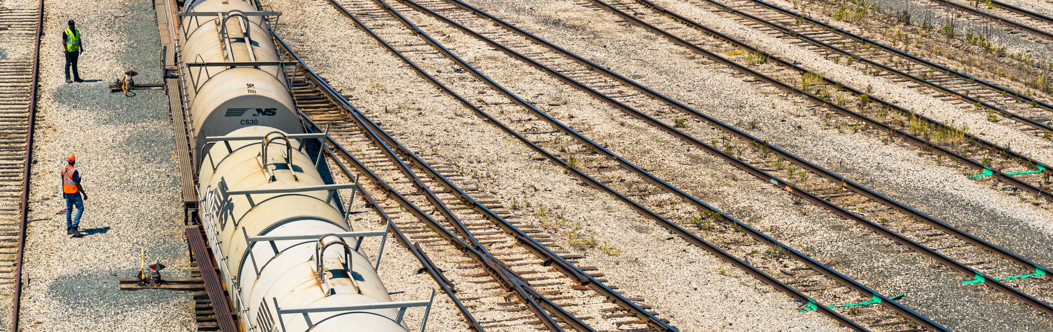 Aerial close up of a train transporting low carbon fuels on a track with two me in safety vests nearby