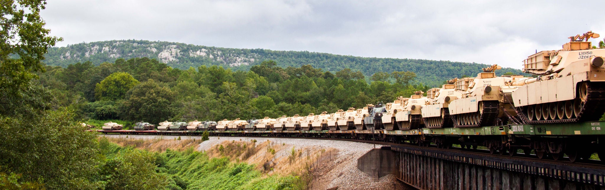 Long shot of tanks and armored vehicles on a train car shipping military equipment